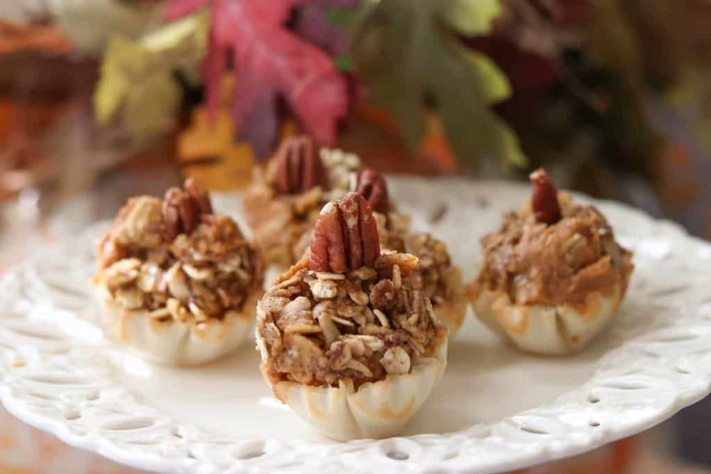 Pumpkin pie tartlets on a cream colored plate with fall leaves in background