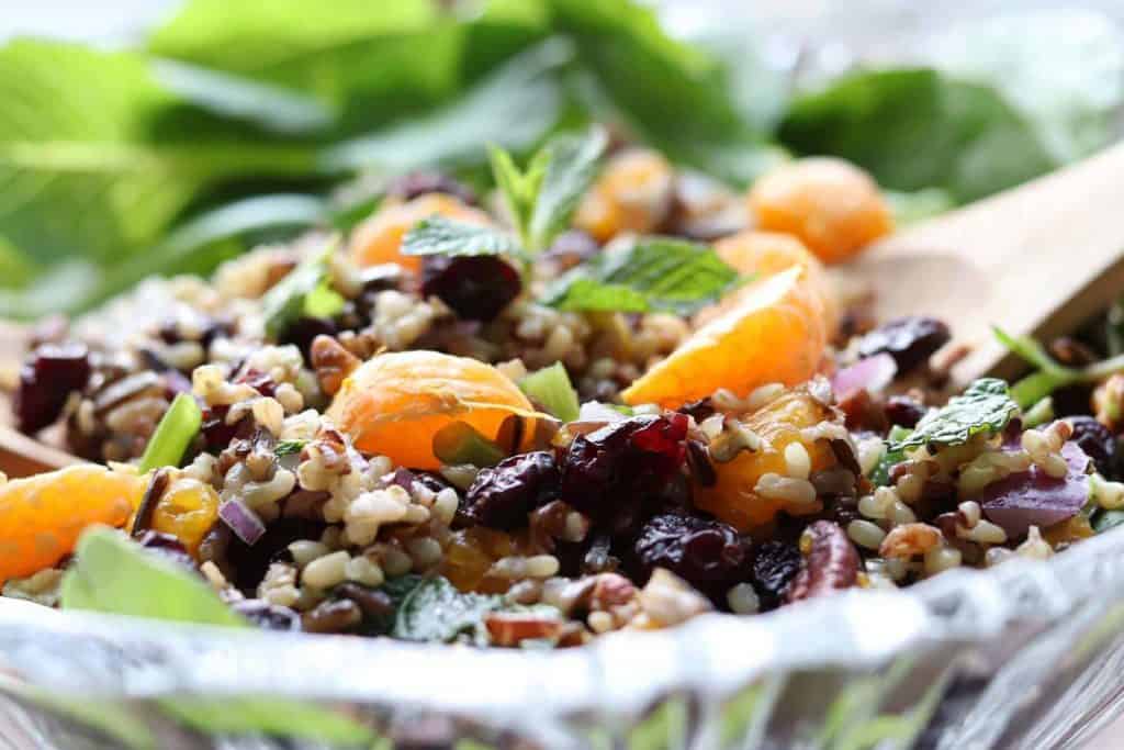 Mandarin Wild Rice Salad with Cranberries, Mint and Pecans in a glass bowl with a wooden spoon from Gourmet Done Skinny