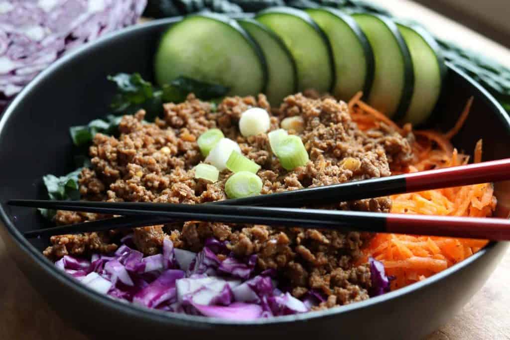 Healthy Instant Pot Korean Beef over kale, cabbage and shredded carrots in a black bowl with Healthy Instant Pot Korean Beef on top on a wooden board from Gourmet Done Skinny