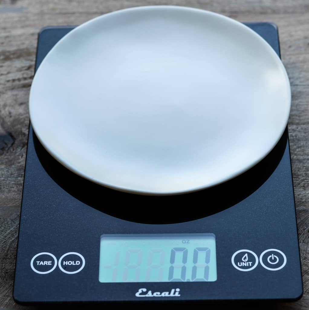 Black digital scale with white plate on a wooden board from Gourmet Done Skinny