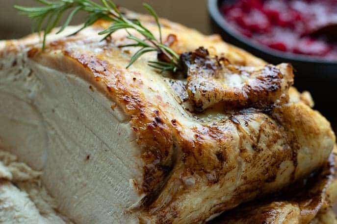 Browned turkey with rosemary, partially sliced and cranberry sauce in the background