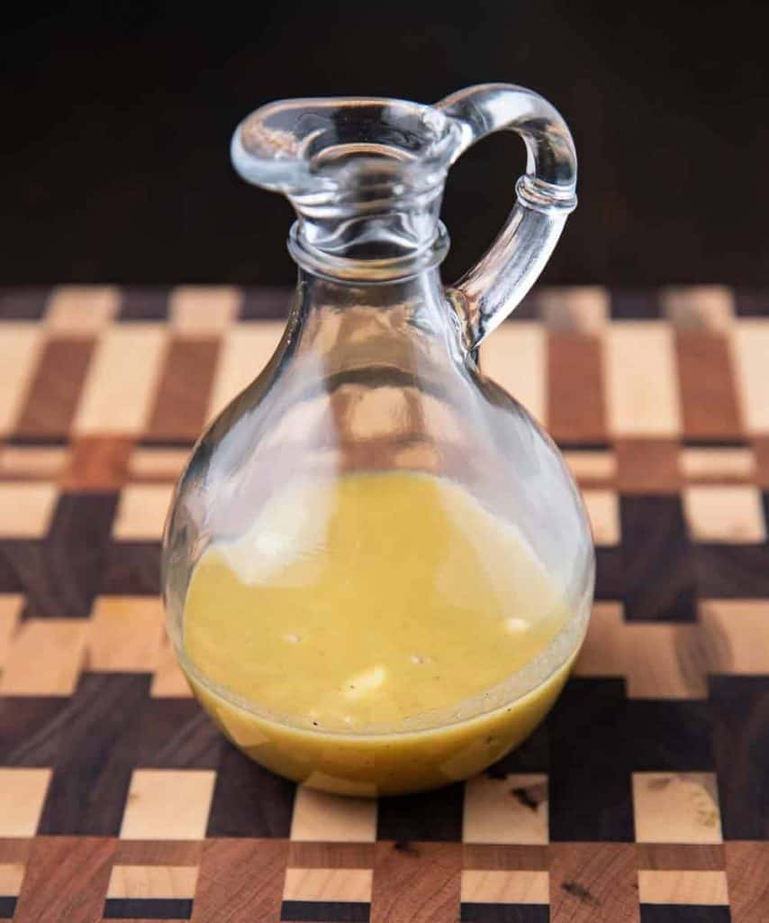 Honey mustard dressing in a glass cruet on a wooden cutting board