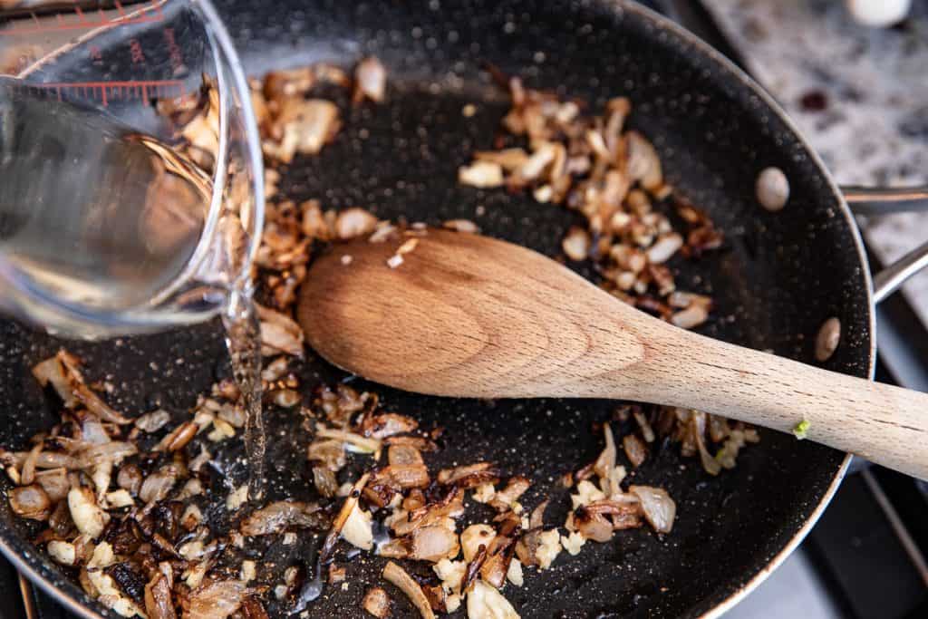 mushroom mixture in a pan with spoon, wine being poured in