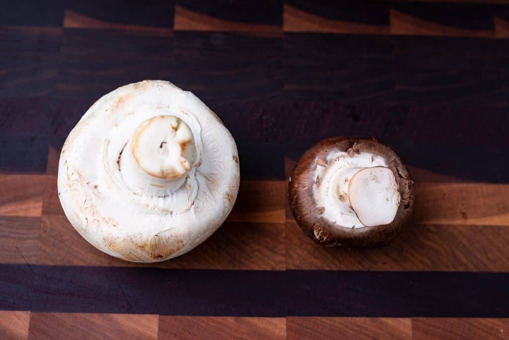 large white mushroom and a small brown mushroom on a board