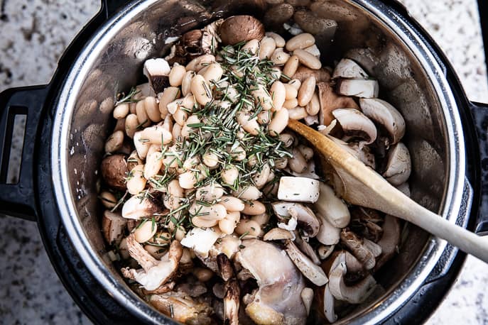 beans, rosemary, mushrooms in an Instant Pot with wooden spoon