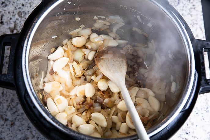 onions and garlic browning in an Instant Pot with a wooden spoon
