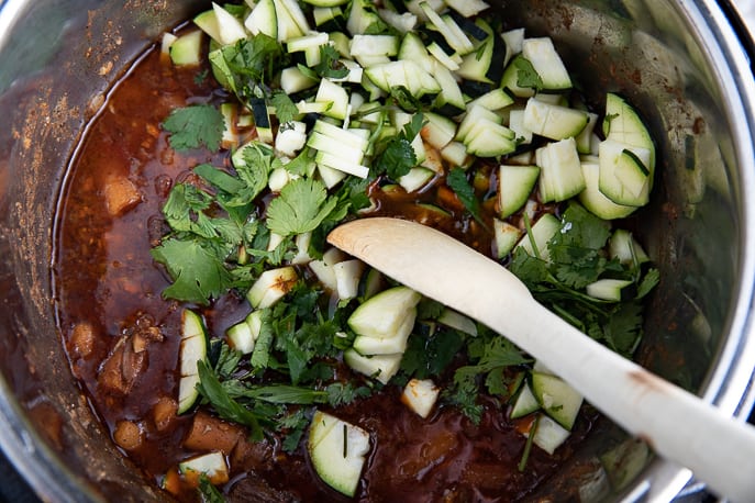 zucchini, cilantro added to lamb curry with spoon