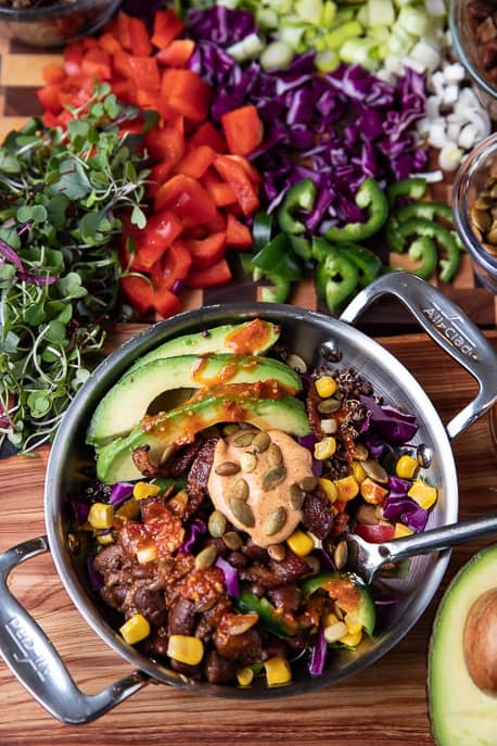 Healthy avocado chile lime bowl in a metal dish on wooden board, vegetables in background