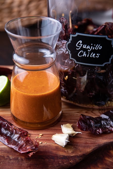Guajillo Chili Lime Vinaigrette in a glass jar with chiles, lime and garlic on a wooden board